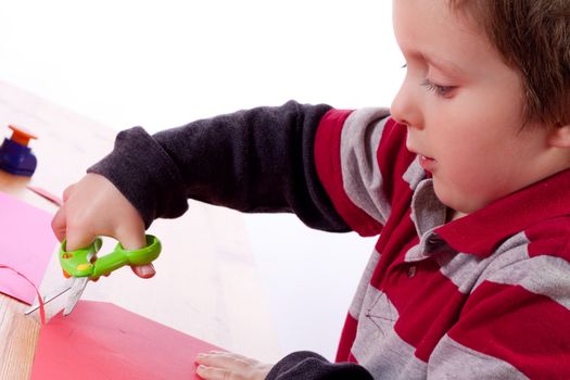 Cute little boy cutting a red heart in cardboard