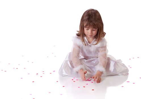 Cute little girl sitting on the floor with heart shaped confetti