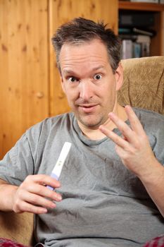 Surprised man holding a positive pregnancy test and showing 3 fingers