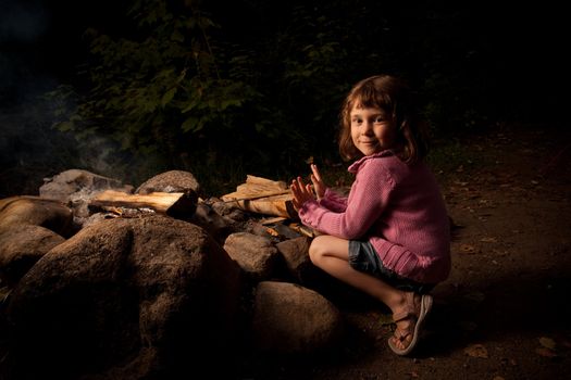 Little girl getting warm near a campfire at night