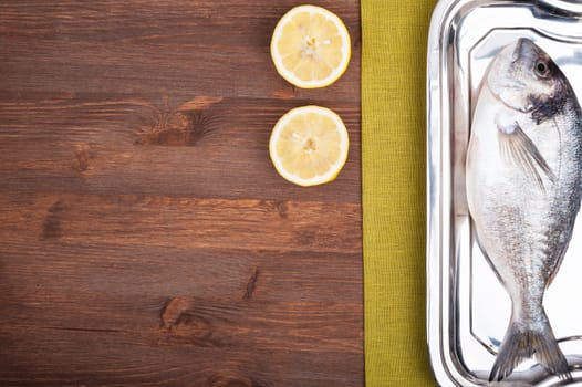 Dorado fish on a wooden surface with slices of lemon