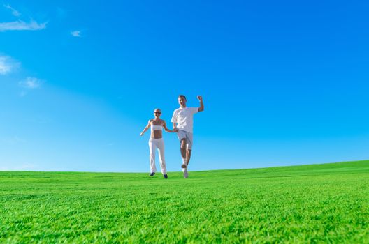 Happy couple jumping together holding hands on a green field