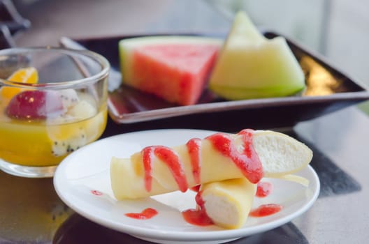 the roll pancakes with the strawberries syrup and cream , fruits on dish  and mix fruits in glass