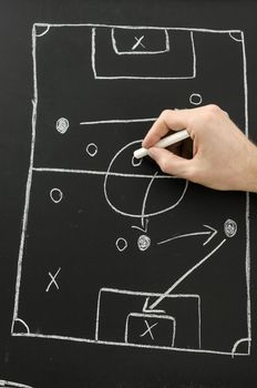 Male hand draws a football play on a chalkboard with chalk. Top view.