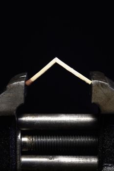 Pressure concept.Cracked match pressured in a bench vice on dark background