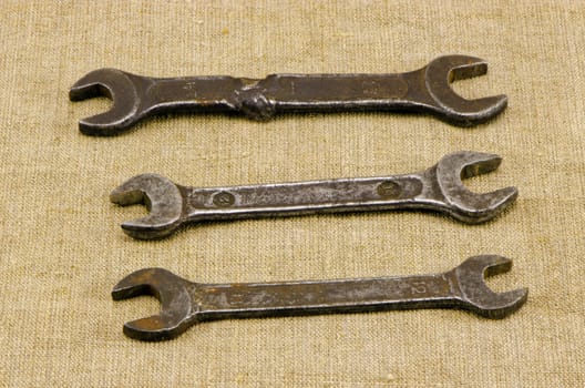 three retro different size screw spanners wrench tools on linen cloth cloth background.