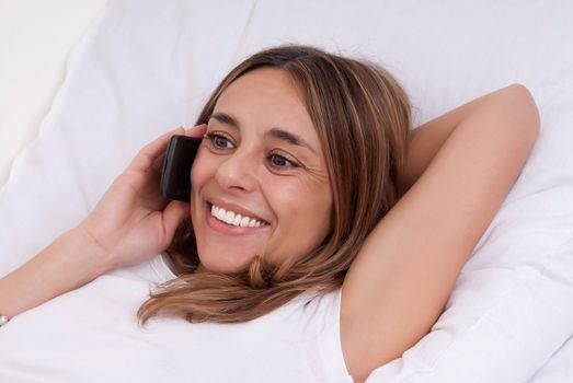 Beautiful happy young woman smiling and using her cell phone at home on her sofa