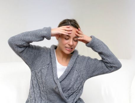 Closeup of pretty young woman suffering from head pain while sitting at home