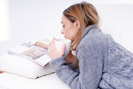 Young happy woman read magazine on sofa in living room