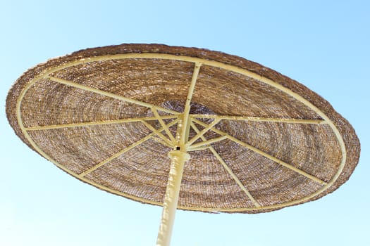 Wicker parasol against blue sky viewed from below.