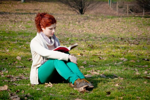 red long hair girl at the park reading in spring 