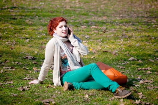 red long hair girl at the park on the phone in spring 