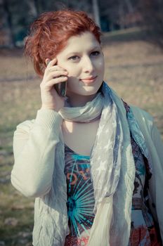 red long hair girl at the park on the phone in spring 