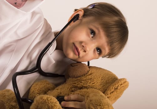 girl in doctors gown is giveing examination to her teddy bear