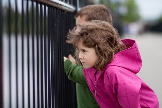 Boy and girl looking through a metal fence