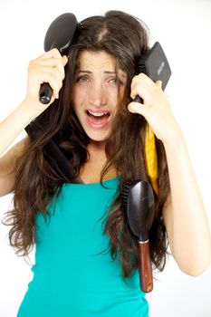 Unhappy young woman with hair tangled in many brushes not able to brush herself
