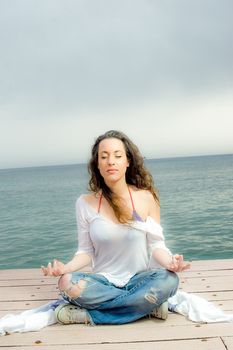 Beautiful girl in meditation on a peer next to the sea