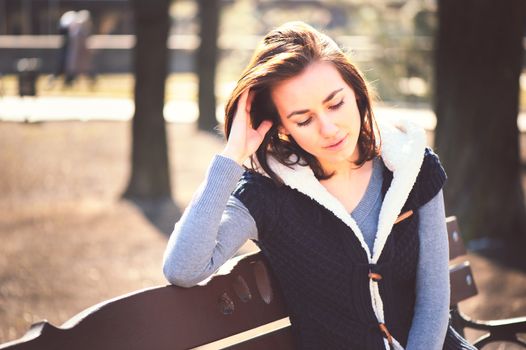 Portrait of young girl sitting on a bench in spring park in sunny day