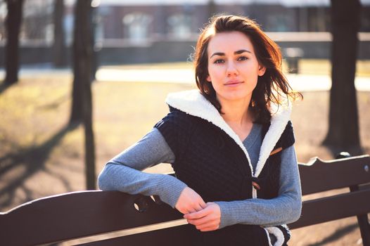 Portrait of young girl sitting on a bench in spring park in sunny day