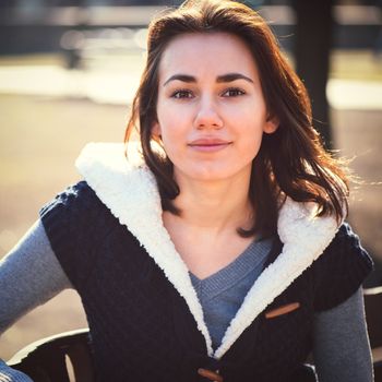 Portrait of young girl sitting on a bench in spring park in sunny day