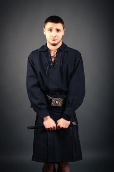 Young drummer in black scottish costume with drumsticks in his hand. Studio shot