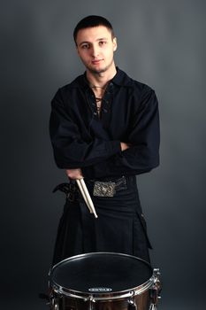 Young drummer in black scottish costume with drumsticks in his hand. Studio shot