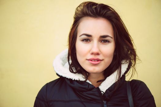 Female brunette fashion model in black jacket in front of yellow wall