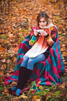 Beautiful girl sitting on armchair in autumn forest with cup in her hands