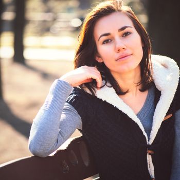 Portrait of young girl sitting on a bench in spring park in sunny day