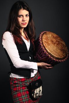 Young girl in scottish costume with djembe. Studio shot