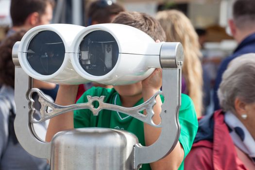 Child looking inside a tourist binoculars next to the sea in Trieste