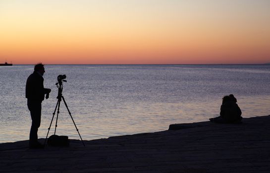 Photographer with camera and tripod take a picture at sunset