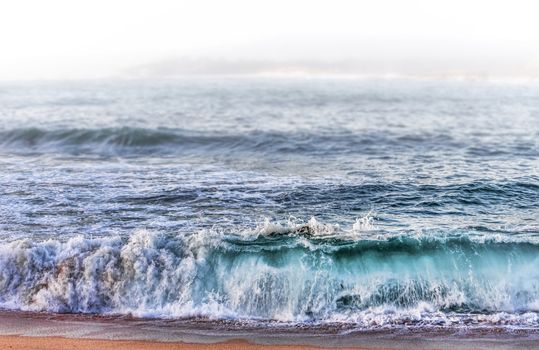 Waves Crashing on Beach at Sunset With Background Fog.