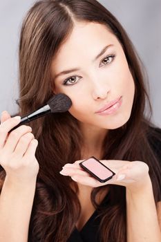 pretty young woman doing make up with powder brush