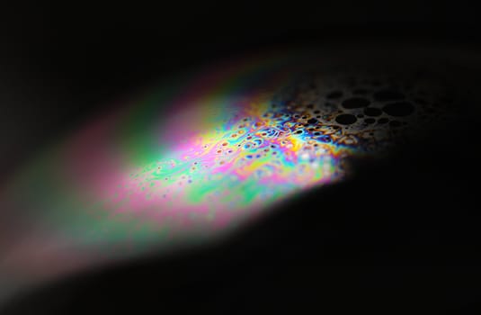 Closeup of a soap bubble. The iridescent colours of soap bubbles are caused by interfering of (internally and externally) reflected light waves and are determined by the thickness of the film. 