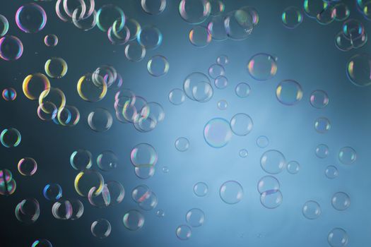 Real soap bubbles floating mid-air over blue background.