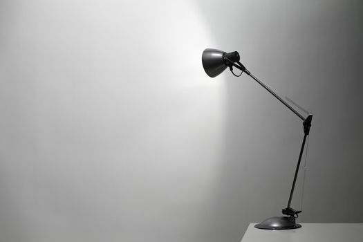 A Grey desk lamp pointed at a grey wall.