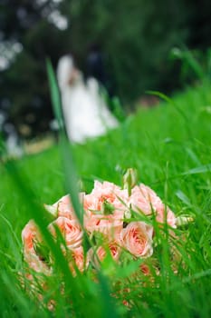 Wedding bouquet of roses laying in grass against enamoured pair