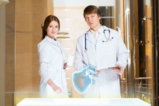 two doctors stand near glowing table discussing. projected objects on a desk