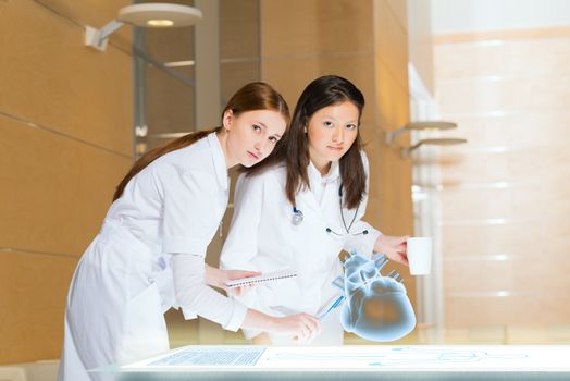 two doctors stand near glowing table discussing. projected objects on a desk