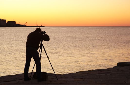 Photographer with camera and tripod take a picture at sunset