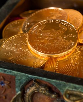 Stacks of gold eagle one troy ounce golden coins from US Treasury mint in old carved pirate treasure chest
