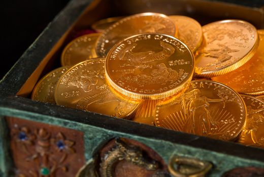 Stacks of gold eagle one troy ounce golden coins from US Treasury mint in old carved pirate treasure chest