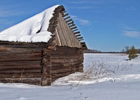 Country view and old wooden barn with a snow-covered sagging roof, winter sunny day