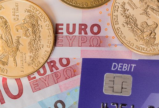 Solid gold coins contrasted with debit word on plastic card on euro note suggesting debt problems