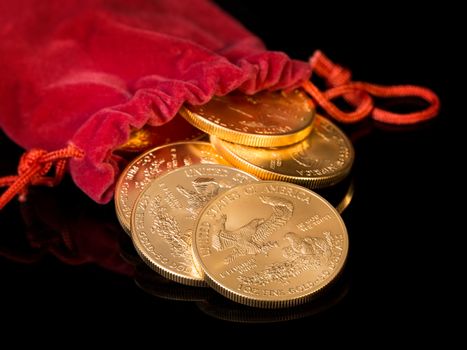 Stacks of gold eagle one troy ounce golden coins from US Treasury mint pouring from mouth of red velvet money bag