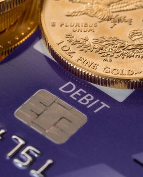 Solid gold coins contrasted with debit word on plastic credit card suggesting debt problems