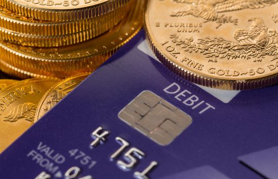 Solid gold coins contrasted with debit word on plastic credit card suggesting debt problems