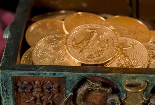 Stacks of gold eagle one troy ounce golden coins from US Treasury mint in old carved pirate treasure chest