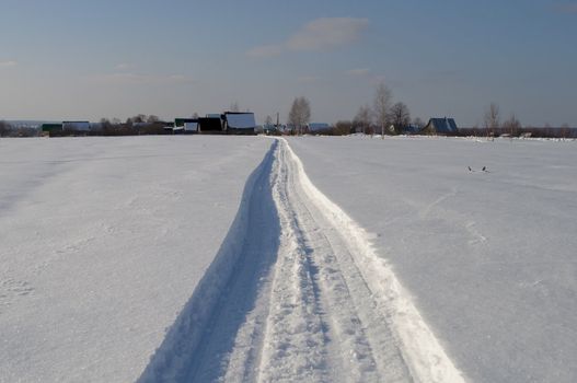 Snowmobile track towards the village, winter sunny day